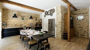 A spacious kitchen with a stone wall, wooden beams, and a dining area with a table set for four.