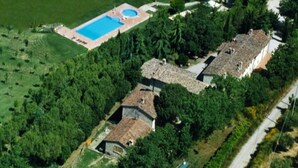 Ovenudblik over en ejendom med swimmingpool, flere bygninger og frodig vegetation.