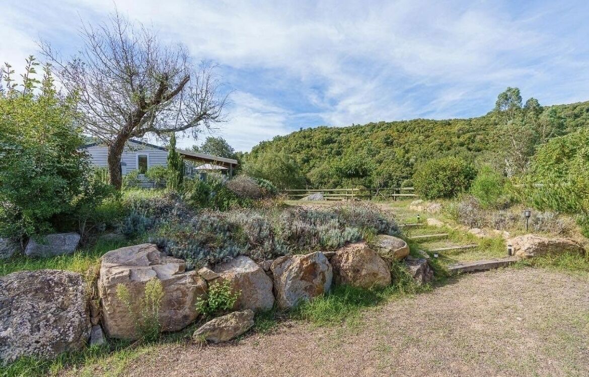 A rustic stone wall, a wooden fence, and a house with a sloped roof in a lush, green landscape.