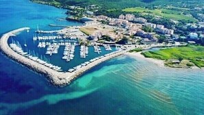 Vista aérea de uma marina costeira com barcos atracados, cercada por vegetação exuberante e montanhas ao fundo.