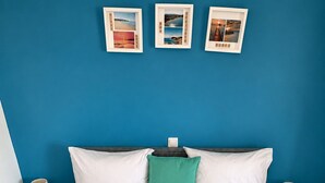 A hotel room with a bed, a blue wall, and three framed pictures.