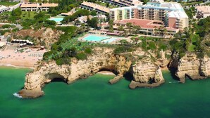 An aerial view of a coastal hotel with a natural rock arch formation, a beach, and a swimming pool. - Kolbast Apartment, balcony, garage (Armação de Pêra)