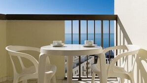 A balcony with white plastic chairs and a table, overlooking a coastal view. - Kolbast Apartment, balcony, garage (Armação de Pêra)