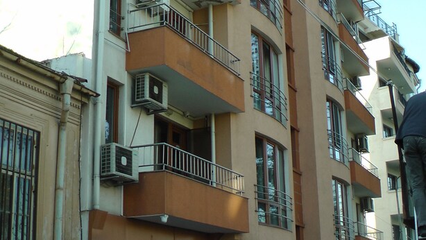 Een meerlaags gebouw met balkons, airconditioners en een etalage met een bord.