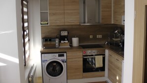 Een kleine keuken met houten kastjes, een ingebouwde wasmachine, een koffiezetapparaat en een oven.