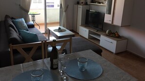 A modern living room with a sofa, TV, and a dining area with a table set for two.
