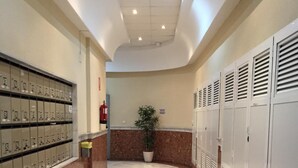 A hallway with lockers, a potted plant, and a fire extinguisher.