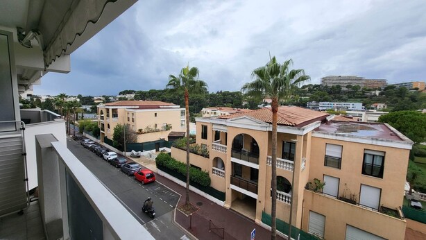 A residential area with multi-story buildings, a street with parked cars, and a motorcyclist. - Apartment T2 air-conditioned, Wifi Fibre, Garage, 4 people (Le Cannet)