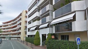 A modern multi-story building with balconies, a pedestrian pathway, and a blue pedestrian crossing sign. - Apartment T2 air-conditioned, Wifi Fibre, Garage, 4 people (Le Cannet)