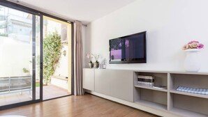 Una sala de estar moderna con un televisor grande, un ventanal corredero que da a un balcón y un diseño minimalista.