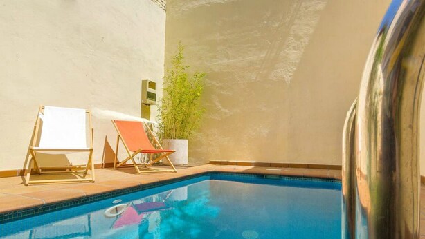 Una piscina con dos sillas de descanso y una planta en maceta.