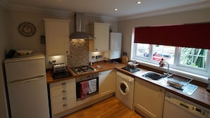 A compact kitchen with a built-in oven, a dishwasher, a sink, and a window with a red blind.