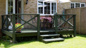 A wooden deck with a table and chairs, a white umbrella, and a brick wall in the background.