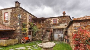 Ein rustikales Steinhaus mit einer Steintreppe, einem kleinen Garten mit einem Steinbrunnen und einem roten Wagen.