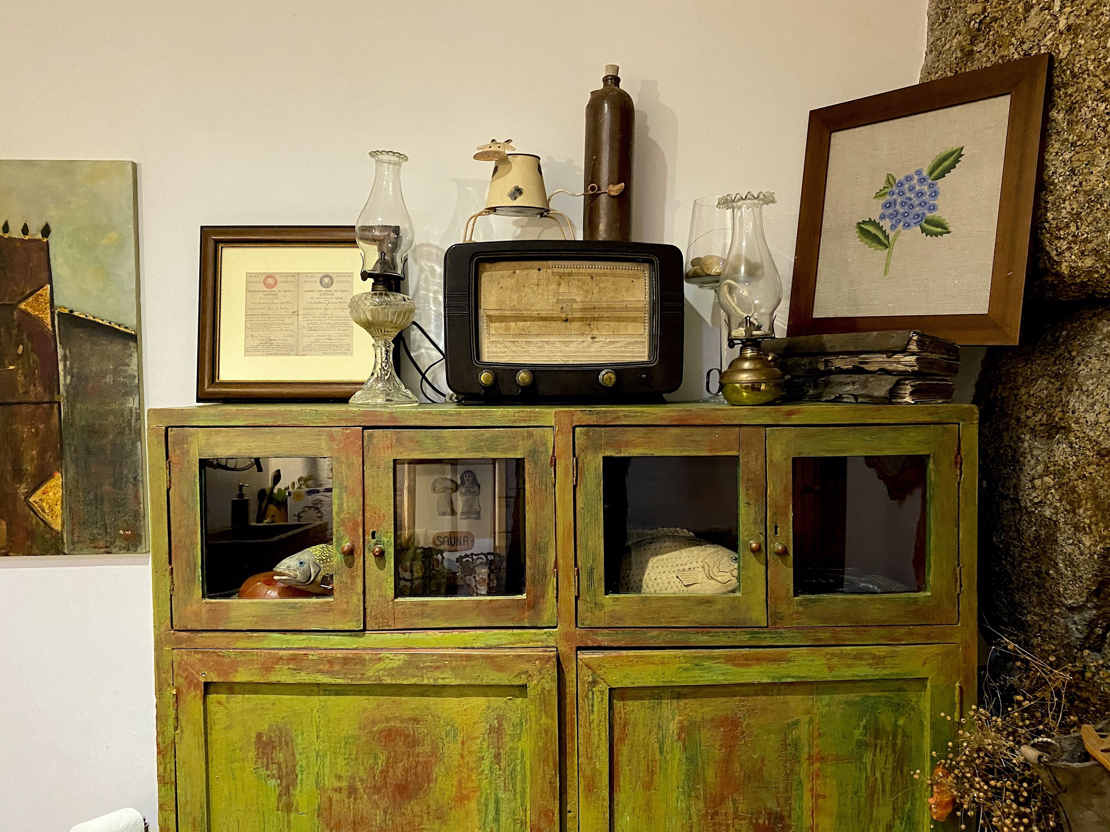 Un mueble antiguo de madera con puertas de cristal, que contiene varios objetos como un diploma enmarcado, una radio antigua y adornos decorativos.