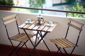 A small wooden table with two chairs, a coffee pot, and two cups on a balcony.