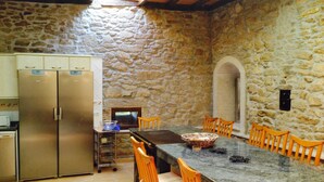 A stone-walled kitchen with a built-in refrigerator, a dining table with chairs, and a stone archway. - Bed Century XII - Pontevedra (Ribeira Sacra) (Fornas - Pontevedra)