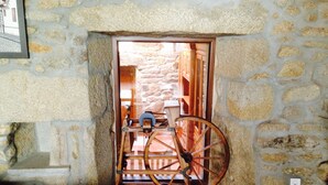 A stone-walled corridor with a wooden cart wheel leaning against the wall. - Bed Century XII - Pontevedra (Ribeira Sacra) (Fornas - Pontevedra)