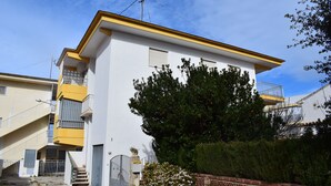 A two-story building with a yellow and white facade, a visible staircase, and a tree in front. - Anacasa Illa de Mallorca Pau Pi AP6320 (Oliva)