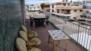 A balcony with wicker chairs and a table, overlooking a residential area with multiple buildings. - Anacasa Illa de Mallorca Pau Pi AP6320 (Oliva)