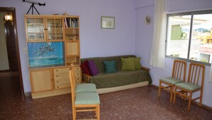 A living room with a sofa, two chairs, a wooden cabinet with glass doors, and a window with a view of buildings. - Anacasa Illa de Mallorca Pau Pi AP6320 (Oliva)