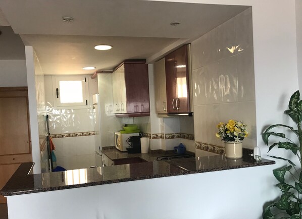 A kitchen with white cabinets, a granite countertop, a microwave, a stove, and a window. - Beautiful apartment on the beachfront (PLAYA-GRAU DE GANDÍA)