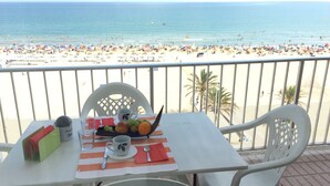 A table with a placemat, a bowl of fruit, a cup, and a spoon on a balcony overlooking a beach. - Beautiful apartment on the beachfront (PLAYA-GRAU DE GANDÍA)