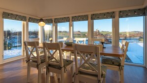 A dining area with a wooden table and white chairs, large windows with a view of a snowy landscape. - Balass Lodge near St. Andrews (Cupar)