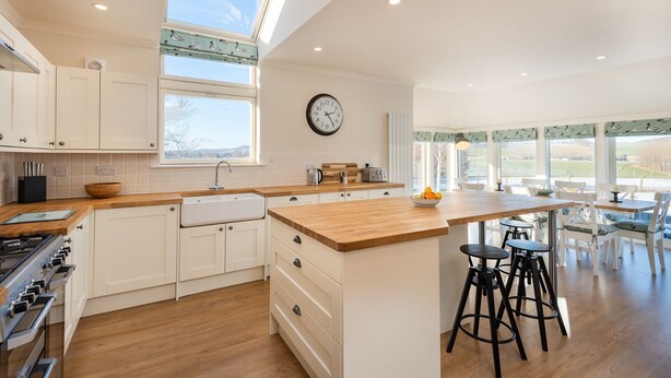A modern kitchen with white cabinets, a wooden countertop, and a large island with bar stools. - Balass Lodge near St. Andrews (Cupar)