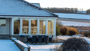 A house with a covered patio, a dining area with chairs, and a view of a snowy landscape. - Balass Lodge near St. Andrews (Cupar)