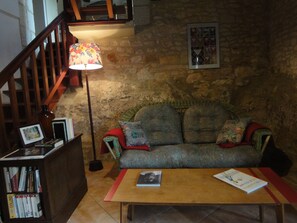 Ein gemütliches Wohnzimmer mit einer Holztreppe, einem Sofa mit gemusterten Kissen, einem Holztisch mit Büchern und einer Stehlampe.