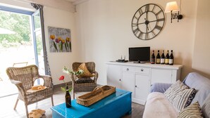 A living room with wicker chairs, a blue coffee table, a sofa, a television, and a wine rack. - Cascina Arcangelo Raffaele, Apartment Gabriele (VERDUNO)