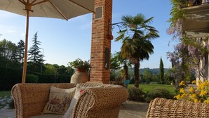 An outdoor seating area with wicker furniture, a brick pillar, and a view of the garden. - Cascina Arcangelo Raffaele, Apartment Gabriele (VERDUNO)