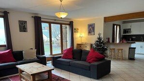 A living room with a sofa, a coffee table, and a small Christmas tree. There is a kitchen in the background with a microwave and cabinets. - Exceptional Cyclist Friendly House, Bourg d'Oisans (Les Bords de Rive)