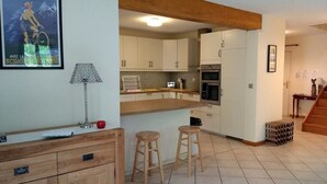 A kitchen with white cabinets, a wooden countertop, and a tiled floor. There are two stools and a lamp on the countertop. - Exceptional Cyclist Friendly House, Bourg d'Oisans (Les Bords de Rive)