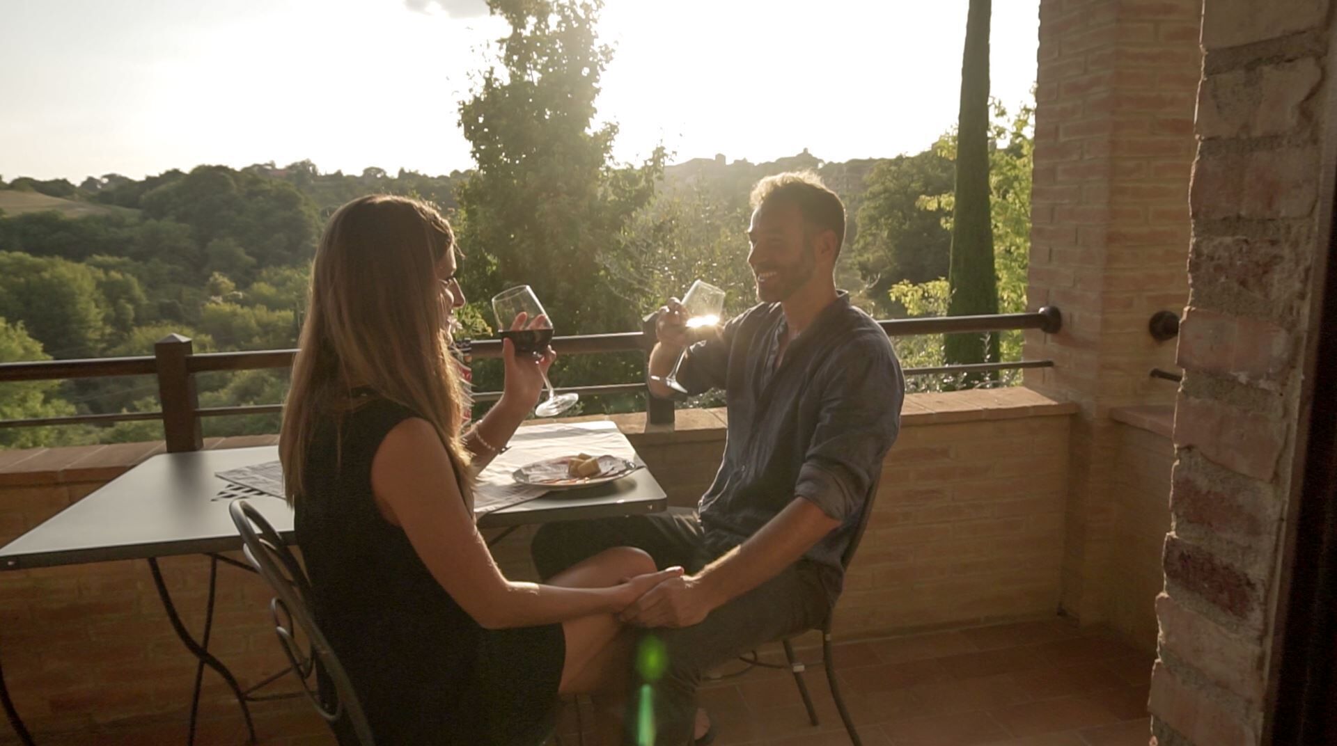 A couple sitting at an outdoor table with a view of a forested landscape.