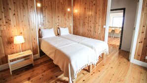 Quarto com painéis de madeira, uma cama de casal, mesa de cabeceira com abajur e porta para outro espaço.