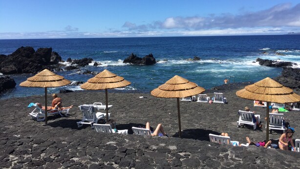 Uma praia com guarda-sóis de palha e espreguiçadeiras brancas.