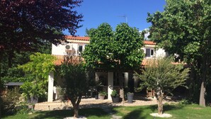 A courtyard with a building featuring a tiled roof, surrounded by trees and potted plants. - Large & beautiful villa on large landscaped fenced garden, large secure pool. (Montpellier)