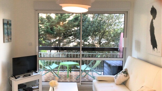 Un salon avec un téléviseur, un canapé blanc et une grande fenêtre donnant sur des arbres.