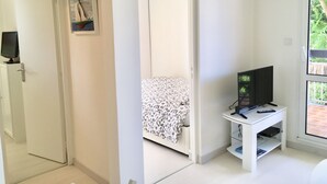 Une pièce comprenant un lit, un téléviseur posé sur un meuble et une porte donnant sur une autre pièce.