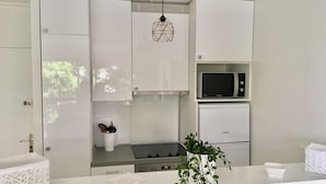 Une cuisine moderne avec des meubles blancs, un four à micro-ondes, un four encastré et un luminaire suspendu.