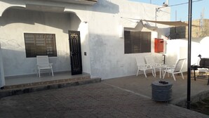 Un bâtiment blanc avec deux portes, une terrasse dotée de chaises blanches et un barbecue.
