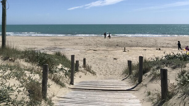 A wooden boardwalk leading to a beach with clear skies and ocean views.
