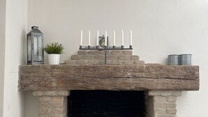 A fireplace with a brick mantle, a white vase with a plant, a lantern, and a row of candles.