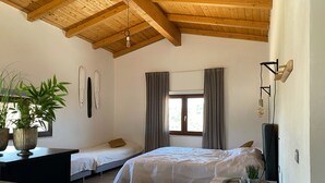 A bedroom with two single beds, a wooden ceiling, a window with curtains, a bedside table with a plant, and a small table with a tray.