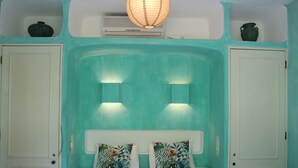 Une chambre avec des murs de couleur turquoise, une tête de lit blanche, deux coussins à motifs floraux et un luminaire au plafond.