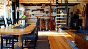 A cozy cabin interior with a wooden dining table, chairs, a spiral staircase, and a fireplace. - Comfortable newly built log cabin in the middle of the forest, built for quality of life and community. (Alfta)
