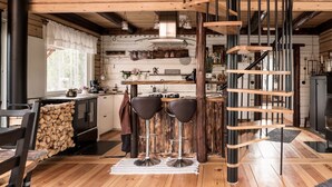 A rustic kitchen with wooden beams, a spiral staircase, and a bar area with stools. - Comfortable newly built log cabin in the middle of the forest, built for quality of life and community. (Alfta)