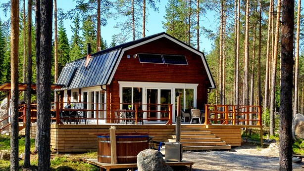 A cabin with a wooden deck, large windows, and solar panels. - Comfortable newly built log cabin in the middle of the forest, built for quality of life and community. (Alfta)
